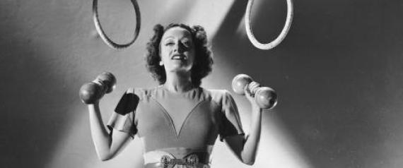 circa 1930:  American actress Gloria Swanson (1899 - 1983) lifts a pair of small weights while a set of rings hang over her head.  (Photo by Ernest Bachrach/John Kobal Foundation/Getty Images)